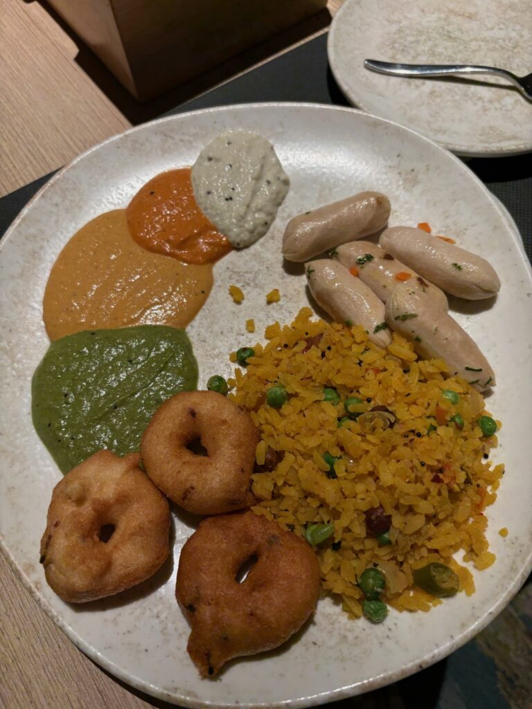 Breakfast buffet plate with Poha, sausages, and chutneys at F5 Restaurant Hilton.