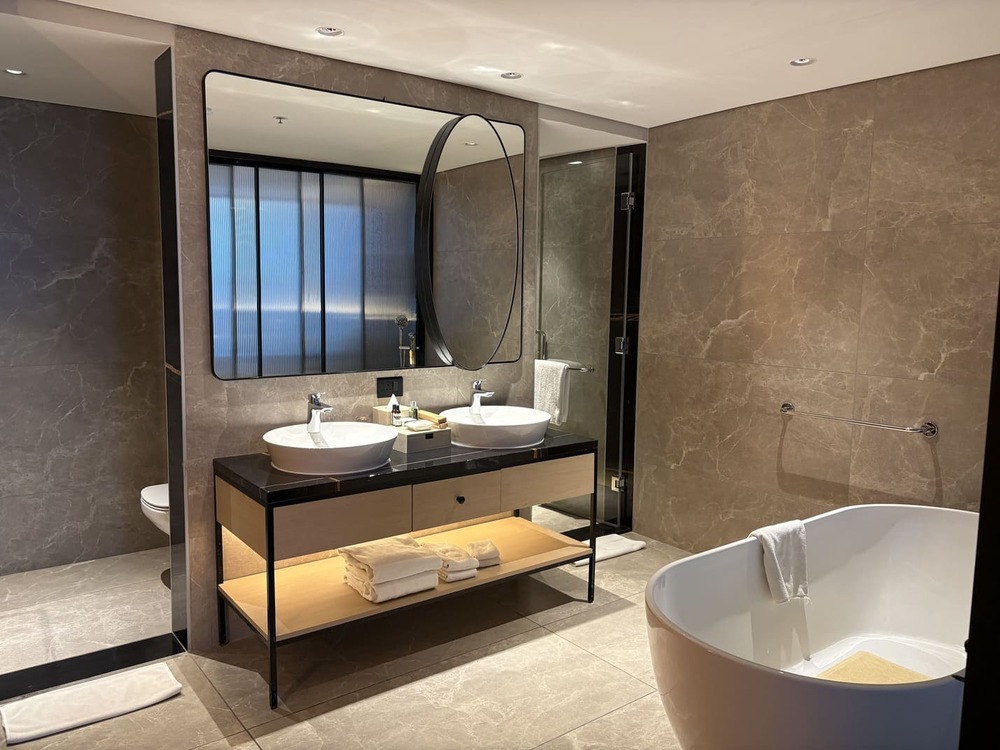 Modern hotel master bathroom featuring a standalone bathtub and double basin vanity mirror layout